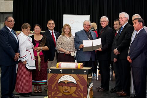 A group of people stand around The Bentwood Box. Two are holding a document in a folder.