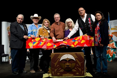 A group of people, including Justice Murray Sinclair, hold a quilt over The Bentwood Box.