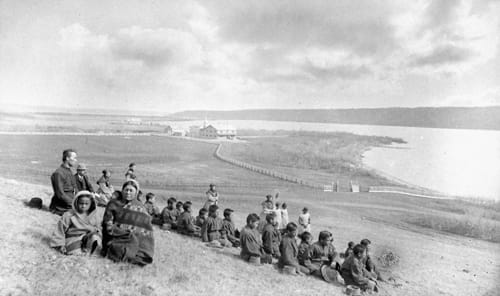 Indigenous students and religious staff sit on a hill overlooking a river near the Qu’Appelle Indian Residential School in Saskatchewan.