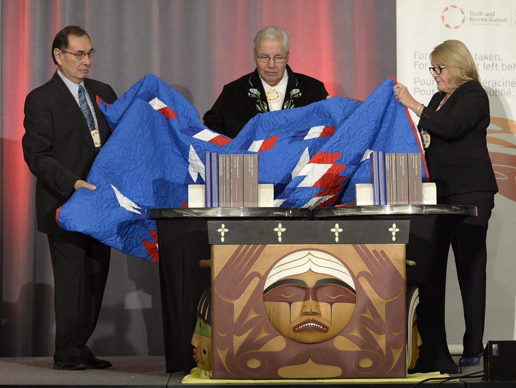 Three people on stage holding blanket by Bentwood Box