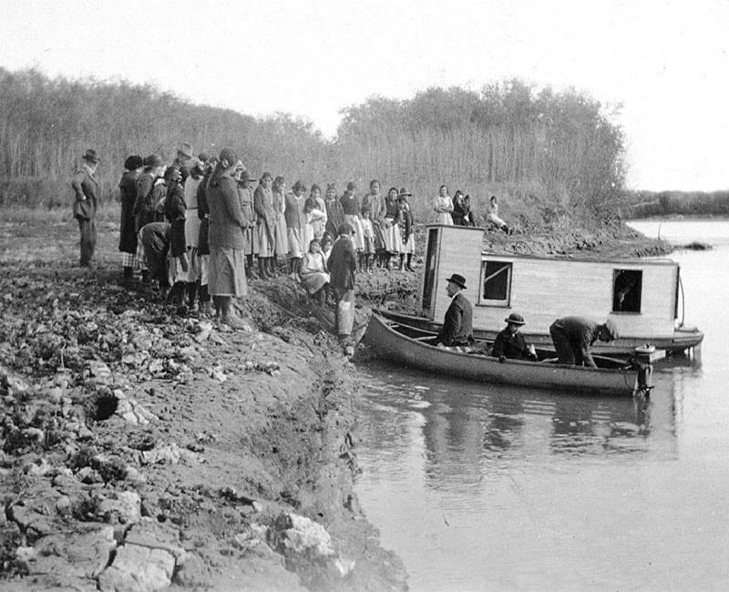 Group of people standing on shore with three people in a boat