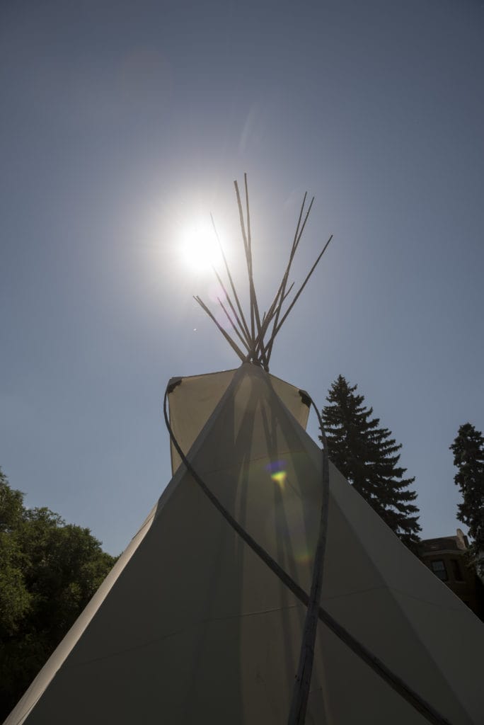 A teepee with the sun shining behind it.