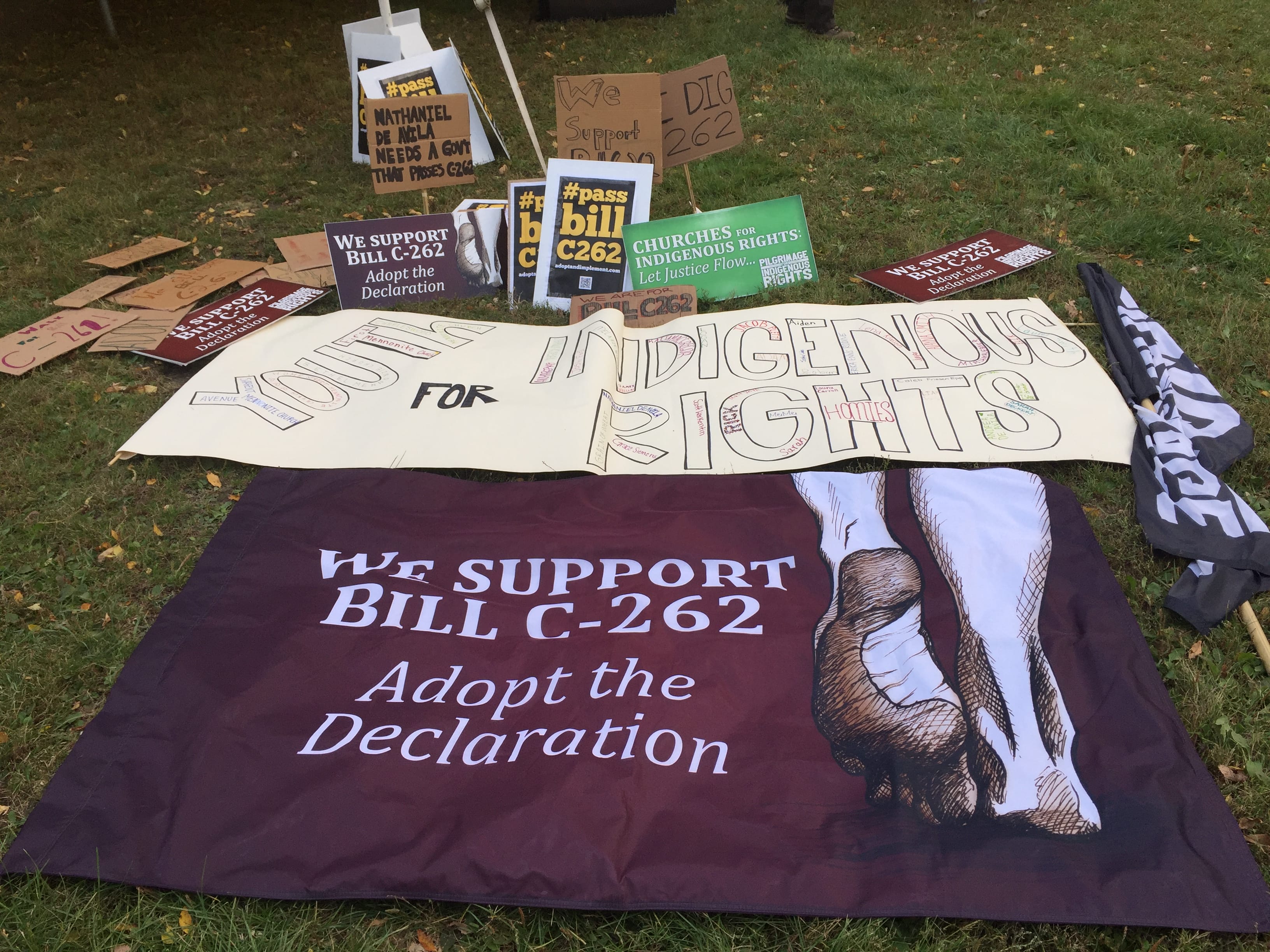 Banners and signs from an event supporting Bill C-262 to adopt UNDRIP rest on grass.