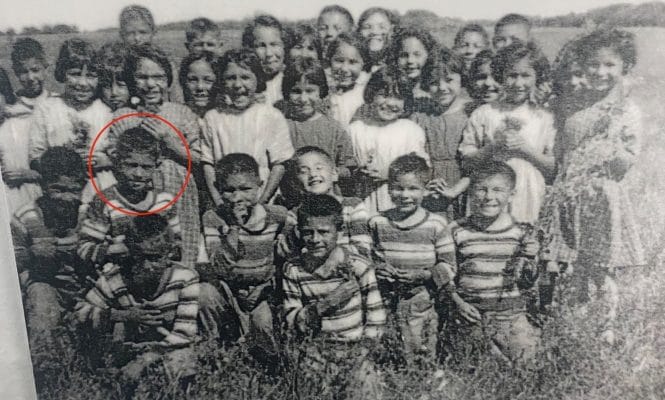 Black and white photo of Eugene Arcand and 32 classmates from St. Michael's Residential School in Duck Lake, Saskatchewan. The children are standing in a field.