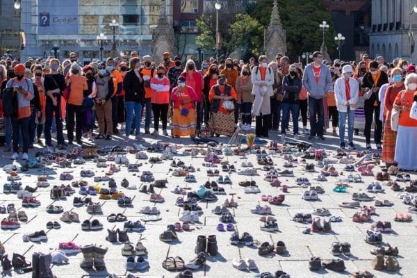 A crowd stands in front of shoes that honour missing and deceased Indigenous children.