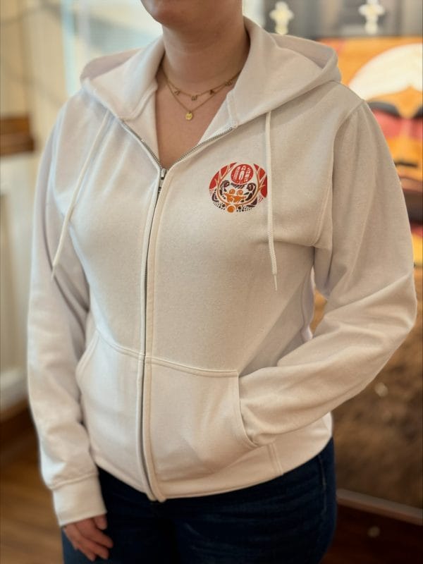 Product image of the front of a white full zip sweatshirt with the survivors flag design on the front and nctr name in French and English across the back