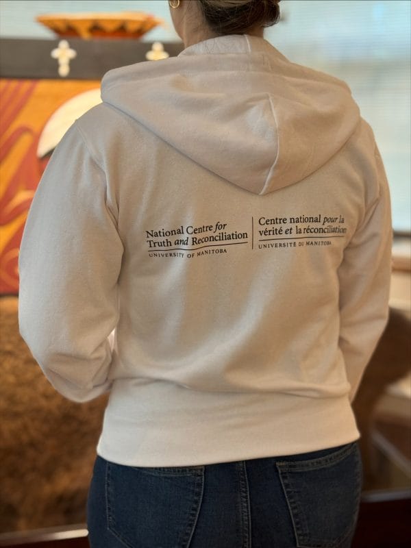 Product image of the rear of a white full zip sweatshirt with the survivors flag design on the front and nctr name in French and English across the back