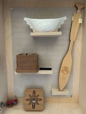 Une collection de trois artefacts comprenant 'Canoë spirituel III,' un canoë en porcelaine de Terry Jackson ; une pagaie de réconciliation de la Pulling Together Canoe Society ; une boîte en bois avec de l'herbe douce tressée et une clé USB et une mini boîte en bois courbé par Shane Jackson présentant un masque de soleil, qui contenait autrefois des documents pour la recherche sur les enfants disparus.